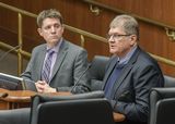 Jim Stark sits at the testifiers' table and speaks to someone out of view. Representative Lippert sits next to him and watches as he speaks.